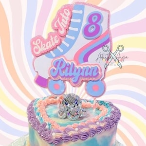 May include: A heart-shaped cake decorated with purple, blue, and white frosting. The cake has a disco ball on top and a roller skate topper that says "Skate Into 8" and "Rilynn". The cake is on a silver cake board with the words "Happy Birthday" written in pink frosting.