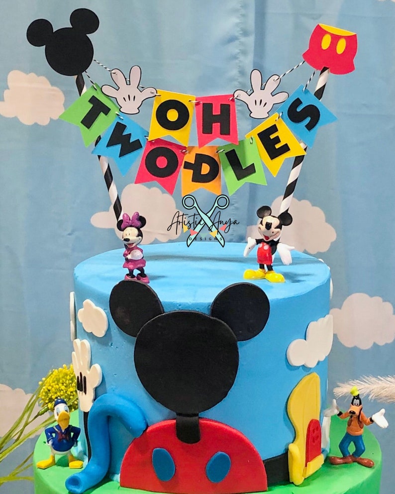 Pu&ograve; includere: Una torta di compleanno a due piani blu e verde decorata con personaggi di Topolino e uno striscione che recita "Oh Two Dles".