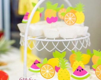 May include: White wire cupcake stand with cupcakes topped with colorful fruit-shaped cutouts. The cutouts include watermelon, orange slices, lemons, cherries, and pineapples. The text "Artistic Anya Designs" is visible.