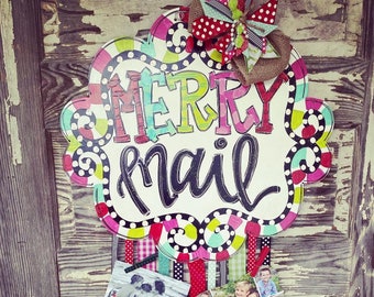 May include: A white, round, wooden sign with the words "Merry Mail" in colorful letters. The sign is decorated with polka dots and colorful ribbons. There are holiday cards attached to the ribbons.
