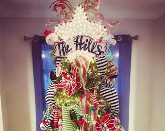 Puede incluir: Un árbol de Navidad decorado con un adorno en forma de estrella que dice "The Hills". El árbol está adornado con adornos rojos, verdes y blancos, cintas a rayas y piernas de elfo. Un adorno de muñeco de nieve está en la base.
