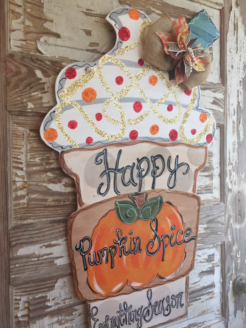May include: A wooden door hanger shaped like an ice cream cone with a white and orange swirl design, glitter, and red polka dots. The cone has a brown base with the text "Happy Pumpkin Spice Everything Season".