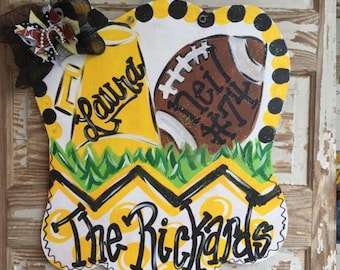 Peut inclure: Un porte-manteau jaune et noir avec un ballon de football, un mégaphone et le texte "The Richards" et "Laura #74".