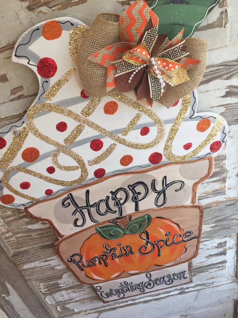 May include: A white and gold glitter pumpkin-shaped door hanger with the text "Happy Pumpkin Spice Everything Season". The hanger is decorated with a brown burlap bow with orange and white polka dot ribbon.