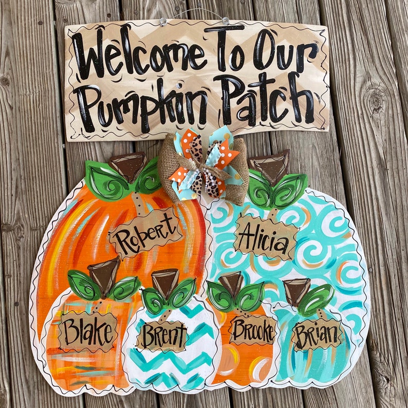 May include: Welcome to our Pumpkin Patch sign with four painted pumpkins. The pumpkins are decorated with orange, blue, and green paint and have names written on them: Robert, Alicia, Blake, Brent, Brooke, and Brian.