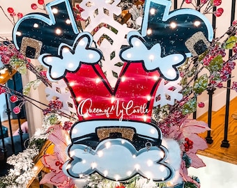 Puede incluir: Decoración navideña con un diseño de Papá Noel y el texto "Queen of My Castle". La decoración es roja, blanca y negra con un copo de nieve y luces. Rodeada de ramas de árbol de Navidad, bayas rojas y cintas.