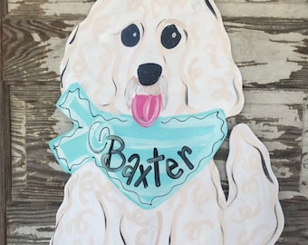 May include: White painted wooden dog door hanger with a blue bandana that says "Baxter" on it.