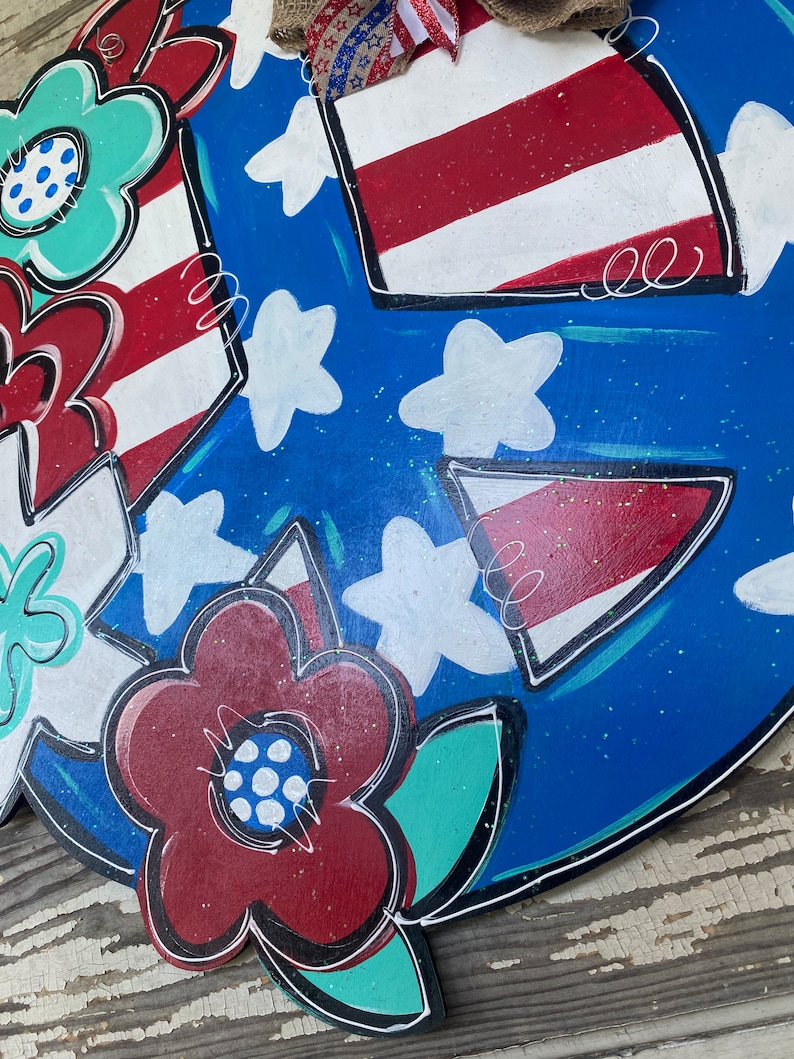 May include: A blue and white peace sign with red, white, and blue stars and stripes. The peace sign is decorated with flowers in red, white, and green.