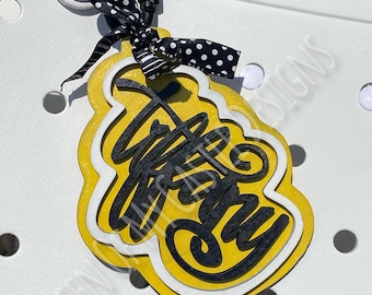 May include: A yellow and black charm with the text "Happy Day" in black lettering. The charm is attached to a black and white polka dot ribbon and a silver carabiner.