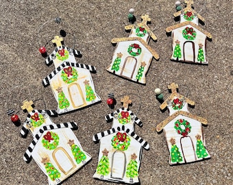 Può includere: Una collezione di sette ornamenti natalizi in legno a forma di chiese. Ogni ornamento presenta una facciata bianca, un tetto a strisce bianche e nere, una ghirlanda verde e alberi di Natale dipinti. Gli ornamenti hanno un gancio di filo e dettagli decorativi.