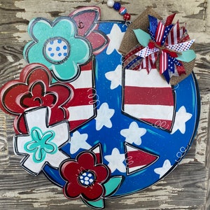 May include: A blue and red peace sign with white stars and stripes. The peace sign is decorated with red, white, and blue flowers and a burlap bow.
