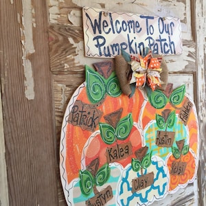 May include: A wooden pumpkin door hanger decorated with fall colors and names, including Patrick, Kalea, Austin, and Kelsi. The sign above reads "Welcome to Our Pumpkin Patch".