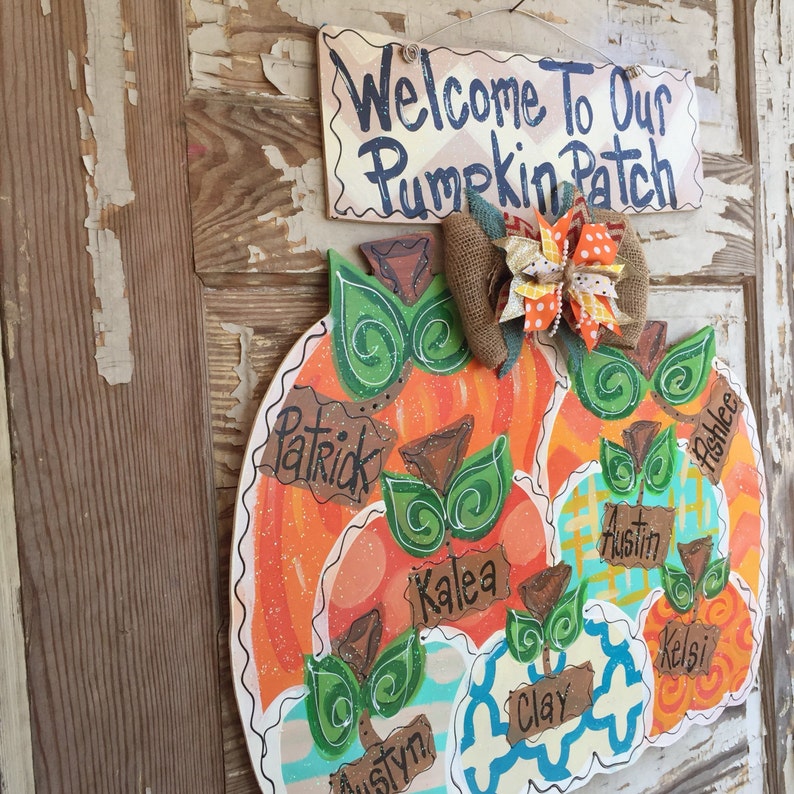 May include: A wooden pumpkin door hanger decorated with fall colors and names, including Patrick, Kalea, Austin, and Kelsi. The sign above reads "Welcome to Our Pumpkin Patch".