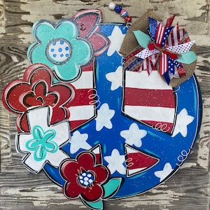 May include: A blue and red peace sign with white stars and red stripes, decorated with red, white, and blue flowers. The peace sign is made of wood and has a rustic look.