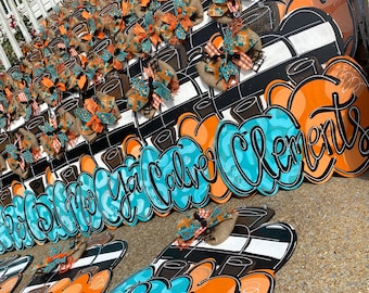 Könnte beinhalten: Ein Stapel orangefarbener und blauer Schilder in Kürbisform mit verschiedenen Namen darauf. Die Schilder sind mit Juteschleifen und schwarz-weißen Streifen verziert.
