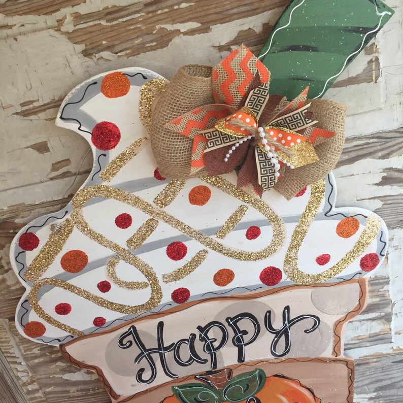 May include: A white and brown door hanger with a pumpkin design and the text "Happy Fall Y'all". The hanger is decorated with a burlap bow and orange and brown ribbon.