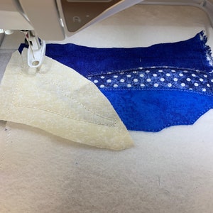 Peut inclure: Gros plan sur l'aiguille d'une machine &agrave; coudre cousant un morceau de tissu. Le tissu est un patchwork de tissus bleus, blancs et cr&egrave;me. La machine est configur&eacute;e pour le quilting.