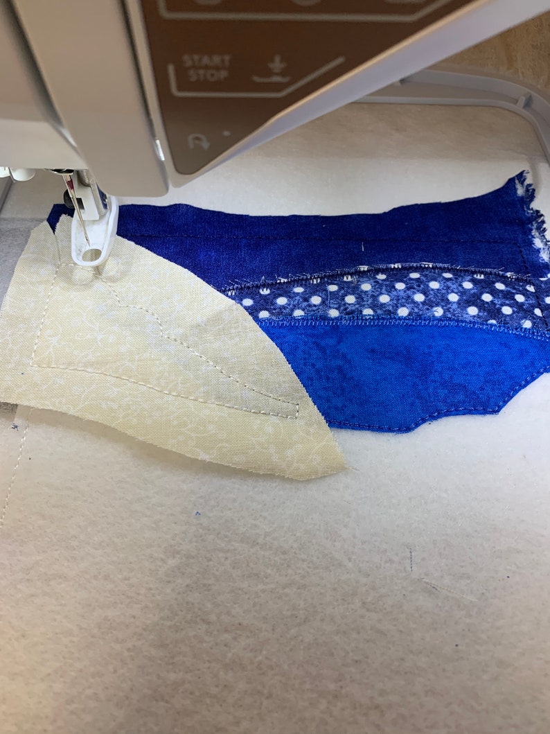 Peut inclure: Gros plan sur l'aiguille d'une machine &agrave; coudre cousant un morceau de tissu. Le tissu est un patchwork de tissus bleus, blancs et cr&egrave;me. La machine est configur&eacute;e pour le quilting.
