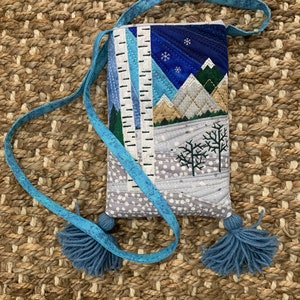 May include: A small, quilted bag with a winter scene design. The bag has a blue strap with tassels and features a snowy mountain landscape with trees and a starry sky.