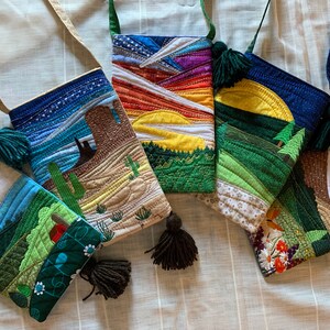 Peut inclure: Cinq sacs matelass&eacute;s color&eacute;s avec diff&eacute;rents motifs de paysages. Chaque sac a un pompon brun et une bandouli&egrave;re. Les motifs comprennent une sc&egrave;ne de d&eacute;sert, un coucher de soleil, une sc&egrave;ne de montagne, une sc&egrave;ne de for&ecirc;t et une sc&egrave;ne de nuage.