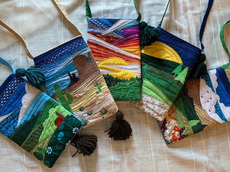 Peut inclure: Cinq sacs matelass&eacute;s color&eacute;s avec diff&eacute;rents motifs de paysages. Chaque sac a un pompon brun et une bandouli&egrave;re. Les motifs comprennent une sc&egrave;ne de d&eacute;sert, un coucher de soleil, une sc&egrave;ne de montagne, une sc&egrave;ne de for&ecirc;t et une sc&egrave;ne de nuage.