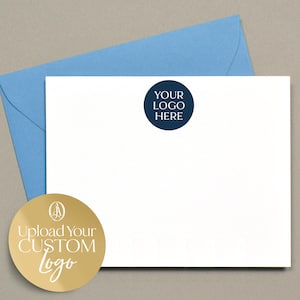 Może przedstawiać: Biały zestaw papierniczy z jasnoniebieską kopertą i ciemnoniebieskim okręgiem z napisem "YOUR LOGO HERE". Dołączona jest również złota naklejka z napisem "UPLOAD YOUR CUSTOM logo".