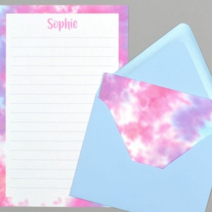 May include: A stationery set featuring a notepad and envelope. The notepad has lined paper with a pink, purple, and blue tie-dye border. The name "Sophie" is written in pink script. The envelope is light blue with a tie-dye pattern on the inside.