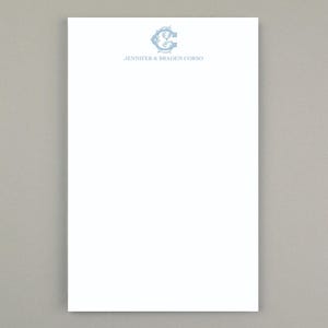 Peut inclure: Papier à lettres blanc avec un monogramme bleu clair et le texte "JENNIFER & BRADEN CORSO" en haut. Le monogramme est un "JC" stylisé avec des fioritures décoratives. Le papier est rectangulaire.