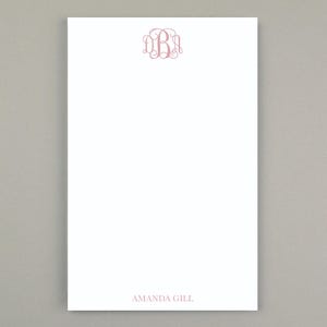 Peut inclure: Bloc-notes blanc avec un monogramme rose en haut au centre et le nom "AMANDA GILL" en bas. Le monogramme est une lettre "B" stylisée avec des volutes décoratives. Le bloc-notes est rectangulaire.