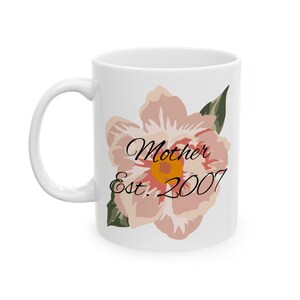 Puede incluir: Taza de cerámica blanca con un gráfico de flor rosa y el texto "Mother Est. 2007".