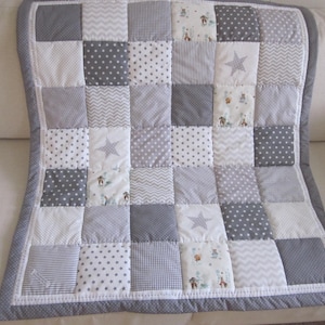 May include: A gray and white patchwork baby quilt with a variety of patterns, including stars, dots, and stripes.