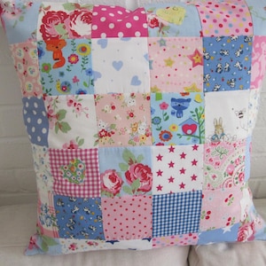 May include: A patchwork pillow cover featuring a variety of colourful fabrics with floral patterns, stars and animal designs. The pillow cover is made up of 16 squares, each with a different pattern.