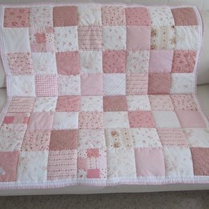 Puede incluir: Una colcha de patchwork que presenta una cuadrícula de parches de tela cuadrados en varios tonos de rosa y blanco. El diseño incluye cuadrados rosas sólidos, cuadrados blancos y cuadrados con patrones florales, de cuadros vichy y rayas, con un borde rosa.