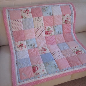 May include: A patchwork quilt with a pink and blue color scheme. The quilt is made of various fabrics with floral, polka dot, and geometric patterns. It is bordered with a pink and white polka dot trim.