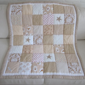 May include: A patchwork quilt featuring a grid of square fabric panels in shades of beige, cream, and white. The design includes various patterns such as damask, small red hearts, stars, chevron, and polka dots, finished with a beige border.