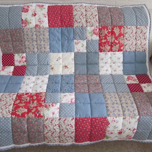 May include: A patchwork quilt with a variety of patterned squares in red, blue, gray, and white. Floral, polka dot, and solid designs are featured. The quilt is approximately 60 inches wide and 70 inches long, with a white border.