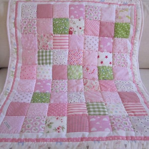 Könnte beinhalten: Eine rosafarbene und grüne Patchwork-Babydecke mit weißem Rand. Die Decke besteht aus verschiedenen Stoffen mit unterschiedlichen Mustern, darunter Punkte, Streifen und Blumen.