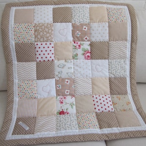 May include: A patchwork quilt with a mix of patterns and colours, including beige, white, and brown squares. Some squares feature heart and star designs. The quilt is edged with a dotted fabric.