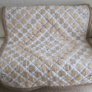 May include: A beige and white checkered quilt with a floral pattern. The quilt is made of cotton fabric and has a brown border.