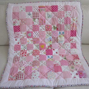 Peut inclure: Une courtepointe patchwork faite à la main dans des tons de rose, blanc et rouge. La courtepointe présente une variété de carrés à motifs, notamment des pois, des rayures et des motifs floraux. Elle a une bordure blanche et un bord à motifs.