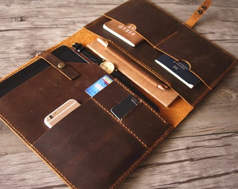 Pode incluir: Um portfólio de couro marrom com vários bolsos e compartimentos. O portfólio está aberto e contém um tablet, um telefone, um caderno, uma caneta, um relógio, cartões de crédito e um passaporte.