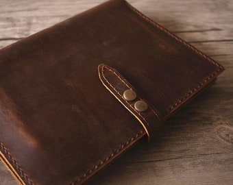 May include: A brown leather journal with a strap closure and two brass rivets. The journal has a distressed look and is made of high-quality leather.