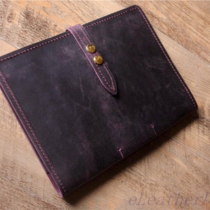 May include: A dark purple leather notebook with a strap and two gold metal clasps. The notebook has a distressed look and is stitched with purple thread.