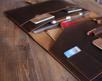 May include: A brown leather portfolio with multiple pockets and slots for carrying documents, pens, and cards. The portfolio is open and shows a laptop, notebook, and credit card inside.