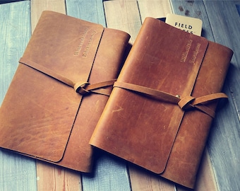 May include: Two brown leather journals with a tied closure. The journal on the left has the text "What words to say Echo in eternity" embossed on the cover. The journal on the right has the text "Weldon & Eva June 2022" embossed on the cover.