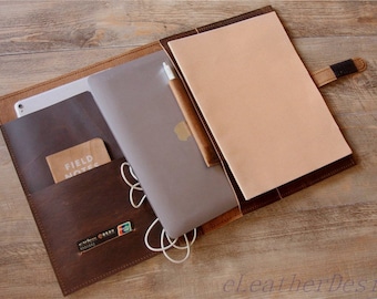 Peut inclure: Un porte-documents en cuir marron foncé doté de plusieurs poches intérieures, un ordinateur portable argenté, un stylet blanc, un carnet beige, un petit livret Field Notes et des câbles de charge blancs. L'étui comprend une fermeture à sangle.