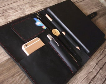 May include: A black leather portfolio with red stitching, featuring a phone, credit cards, a pen, a pencil, and a watch.