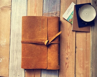 May include: A brown leather-bound journal with a personalized inscription that reads "Evan Matthew Ives April 9 2023". The journal is closed and has a leather strap with a knot.