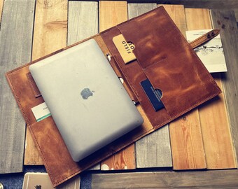 Pode incluir: Uma capa para laptop de couro marrom com vários bolsos e uma alça. A capa está aberta e um laptop está dentro. A capa está sobre uma superfície de madeira.