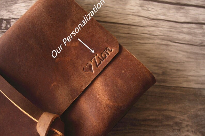 May include: A brown leather journal with a strap closure. The journal is personalized with the name "Zion" in a heart shape.